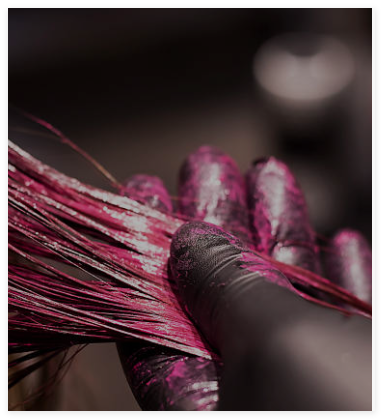 A hairstylist’s hand applying color to hair, demonstrating the hair dyeing process and coloring technique.